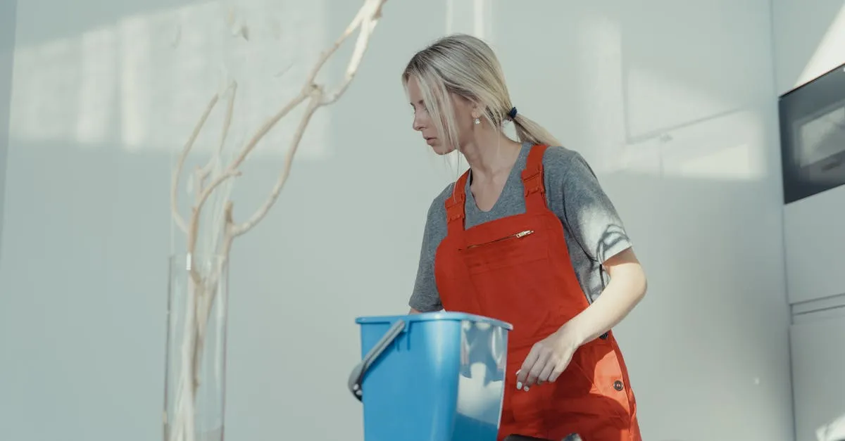 A woman in a red uniform cleans indoors with a blue bucket, ensuring a spotless environment.